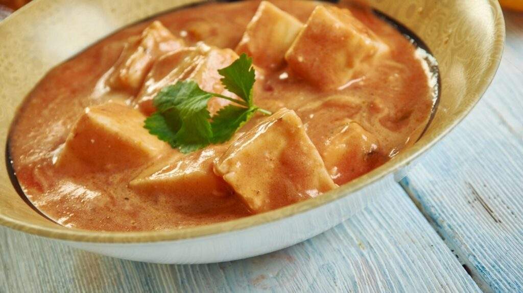 An image of a bowl of Chaman with golden-fried paneer cheese in a creamy tomato-based gravy, garnished with fresh cilantro leaves.